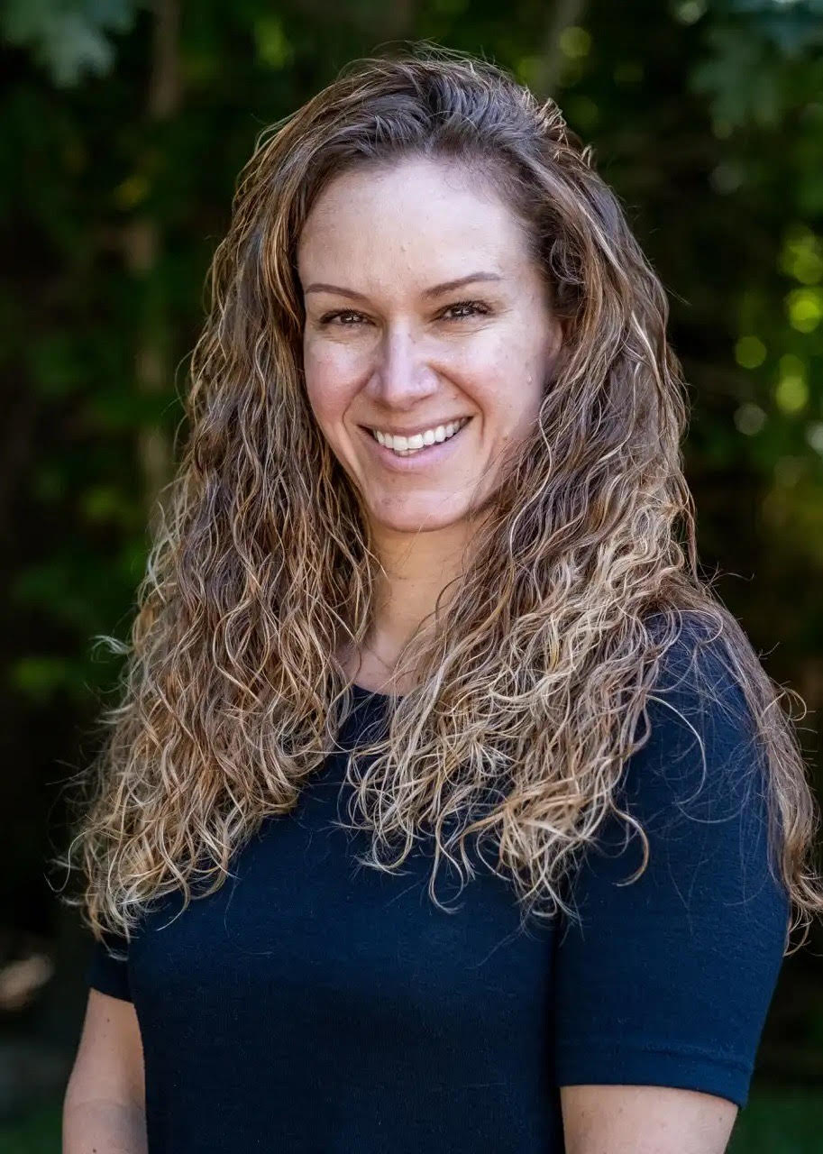 Photo of curly haired woman standing in front of trees