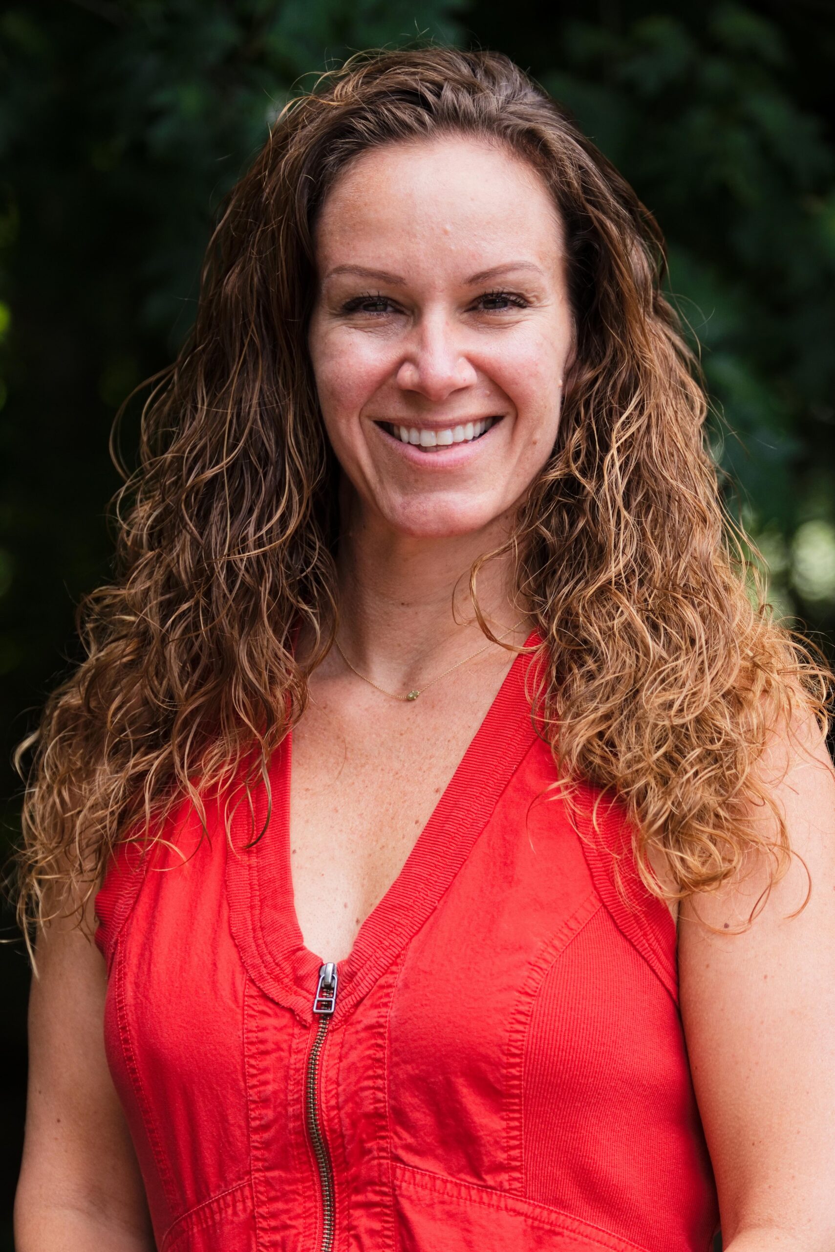 Photo of curly haired woman standing in front of trees